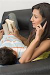 Side profile of a young woman talking on a mobile phone with a young man reading a book