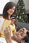 Young woman talking on a mobile phone beside a young man reading a book