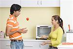 Side profile of a young couple playing with a tomato in a kitchen