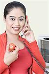 Portrait of a young woman talking on a telephone and holding a tomato