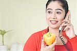 Young woman talking on the telephone and holding a yellow bell pepper