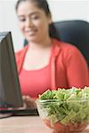 Gros plan d'un bol de salade avec une jeune femme à l'aide d'un ordinateur à l'arrière-plan