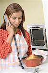 Junge Frau hält einen Kuchen in einem Werkzeug und Gespräch am Telefon