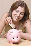 Close-up of a young woman inserting money into a piggy bank