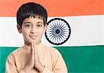 Close-up of a boy standing in front of the Indian flag with his hands folded
