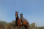 Low angle view of a teenage girl riding a horse and holding a pair of binoculars