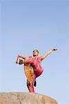 Low angle view of a young woman performing Bharatnatyam on a rock