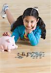 Portrait d'une jeune fille allongée sur le sol et mettre les pièces de monnaie dans une tirelire