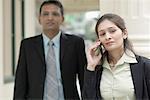 Gros plan d'une femme d'affaires parlant sur un téléphone mobile avec un homme d'affaires debout derrière elle