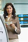 Gros plan d'une femme d'affaires debout devant une machine automatique de billet et la tenue de sa carte d'embarquement