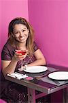 Portrait of a young woman sitting in a restaurant and holding a martini