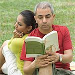Gros plan d'un homme adult mid, lire un livre avec une femme adulte moyenne assis derrière lui
