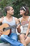 Close-up of a young man playing a guitar with a mid adult woman sitting beside him