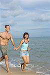 Mid femme adulte et un jeune homme en cours d'exécution sur la plage et souriant