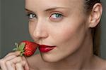 Young woman with a red strawberry under her red lips (part of), close-up