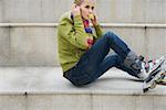 Young woman wearing inline skates listening to music about earphones sitting on staircase
