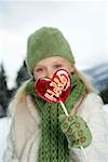 Girl holding a heart-shaped lollipop at camera