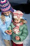 Two girls wearing warm clothing holding a burning candle