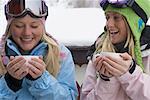 Two young blonde women in ski-wear holding cups of hot chocolate