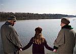 Grandparents holding hands with granddaughter (10-12) by river