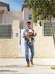 Father looking at camera with 5 month old baby in sling, urban location, Alicante, Spain,