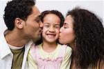 Father and mother kissing daughter on cheek