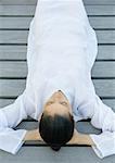 Woman lying on decking, hands behind head, high angle view