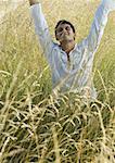 Man standing in field, raising arms, eyes closed