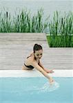 Woman leaning against edge of pool, touching surface of water, lake in background