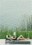 Frau liegend auf Lounge-Sessel, lesen, neben See