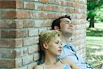 Couple sitting outdoors, leaning against brick wall