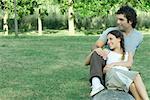 Couple sitting on log, woman leaning against man, both looking away