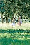 Young women running through field, holding hands