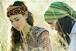 Two young women sitting in field, looking down