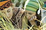 Two young women lying in field, one listening to headphones, close-up