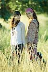 Young hippie women standing in field, one holding guitar and smiling at camera