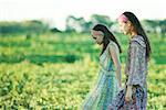 Young hippie women walking through field, side view