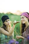 Two young women outdoors, one holding dandelion seed head on palm of hand