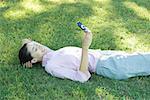 Businesswoman lying in grass, looking at cell phone, smiling