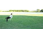 Businessman sitting in chair on lawn, hands in pockets, looking up