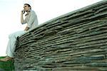 Businesswoman sitting on stone wall, using cell phone, low angle view