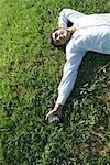 Businessman lying on grass, holding cell phone, eyes closed, smiling
