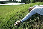 Businessman lying on grass, holding cell phone