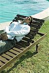 Businessman reclining in lounge chair near pool, holding laZSop on lap