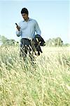 Businessman standing in field, looking at cell phone