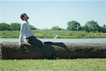 Businessman sitting on tree trunk with laZSop, looking up