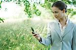 Businesswoman standing in field, looking at cell phone