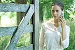 Woman standing by wood gate, using cell phone