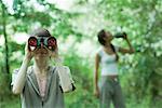 Woman looking through binoculars while friend drinks water in background