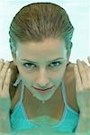 Jeune femme à la piscine, les mains par le côté du visage et du visage ruisselant